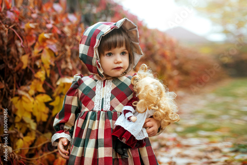 Little pretty girl in vintage dress with a porcelain doll in the autumn park