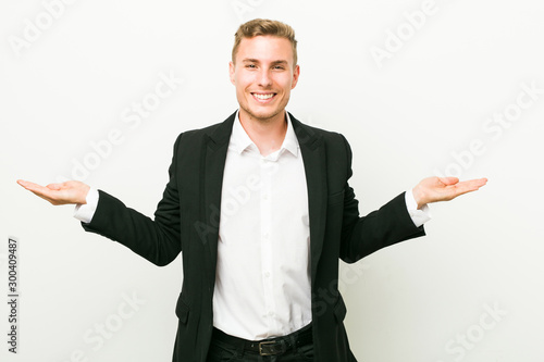 Young caucasian business man makes scale with arms, feels happy and confident.