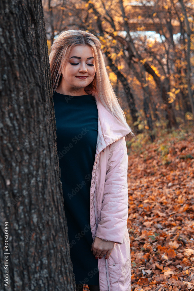 Beautiful woman looking out from behind tree. Pretty calm woman touching tree and looking at camera in quiet forest Beautiful woman looking out from behind tree. Pretty calm woman touching tree and looking at camera in quiet forest