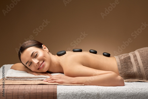 wellness, beauty and relaxation concept - smiling beautiful young woman having hot stone massage at spa