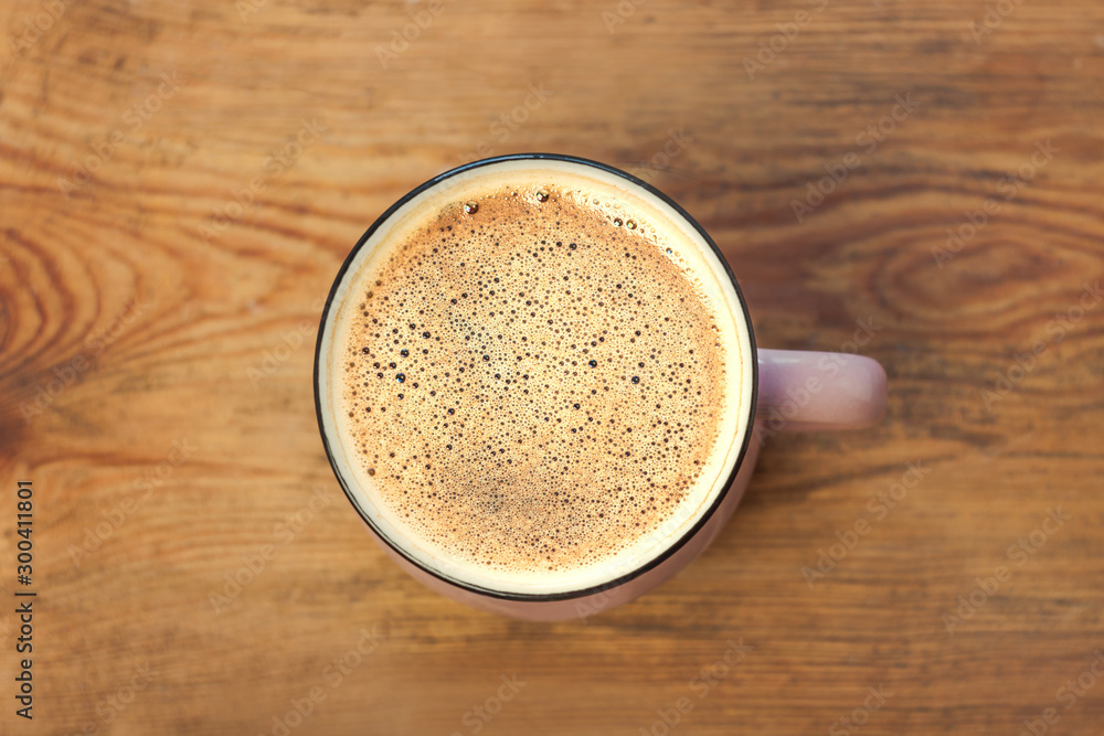 A cup of coffee with beautiful foam on a brown wooden background. Warm colors, stylish toning. A cup of coffee with beautiful foam on a brown wooden background. Warm colors, stylish toning.