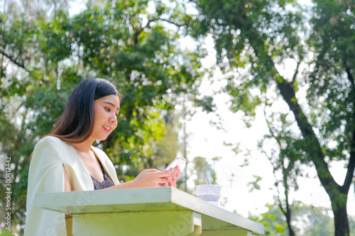 Asian beautiful working woman use mobile phone to work with her business in the garden with morning soft light.