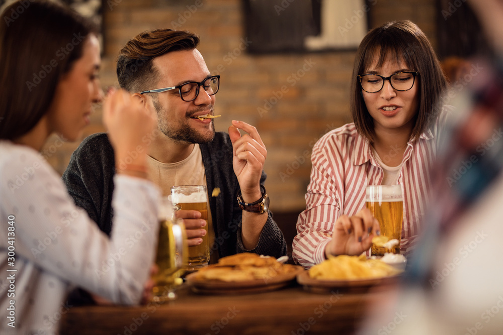 Young couple eating nacho chips and drinking beer with friends in a bar.