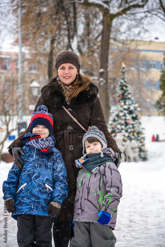 Family portrait of a smiling mother hugging a boy and his sibling brother. Wearing winter warm clothes walking winter city streets