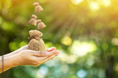 Women hands hold a money bags and dropping on the top in the public park for loans to planned investment in the future concept.