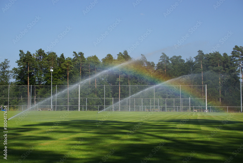 Naklejka stationäre Rasensprenger auf dem Sportplatz erzeugen Regenbogen