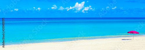 Pink beach umbrella parasol on the tropical beach. Vacation background. Idyllic beach landscape. Wide banner format