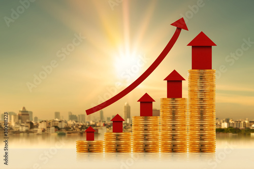 Stack gold coin and red home model put on the top and a arrow graph with growing value on photo blur cityscape background, Business investment  for real estate concept.