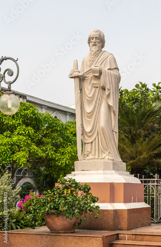 Canvas Print Da Nang, Vietnam - March 10, 2019: Closeup of cream-colored statue of Saint Paul with his sword and epistle backed by green foliage and under silver sky