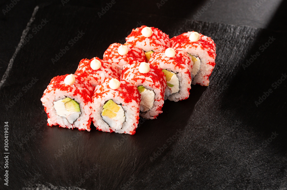 Sushi Rolls with avocado, shrimp and cream cheese inside on black slate isolated. California rolls covered orange tobiko or masago caviar. Sushi menu. Horizontal photo. Sushi Rolls with avocado, shrimp and cream cheese inside on black slate isolated. California rolls covered orange tobiko or masago caviar. Sushi menu. Horizontal photo.