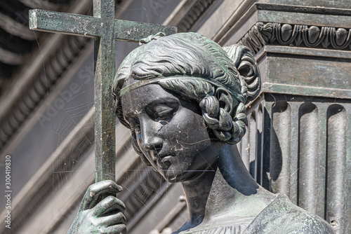 Photography Old metal statue of a sensual woman as a prayer with a cross and covered with sp
