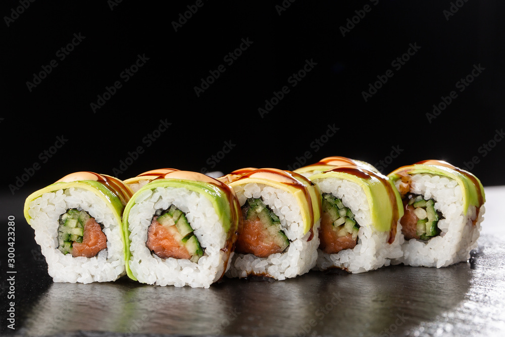 Green dragon sushi roll with salmon, cucumber and avocado. Japanese food. Traditional asian rice sushi healthy seafood. Black background. Horizontal photo. Green dragon sushi roll with salmon, cucumber and avocado. Japanese food. Traditional asian rice sushi healthy seafood. Black background. Horizontal photo.