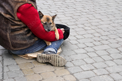 A homeless man sitting on the sidewalk warms the dog in his arms.  concept of poverty, love and warmth