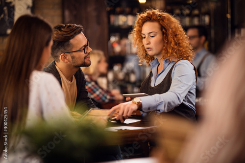 Young waitress communicating with a couple while taking their order in a bar.