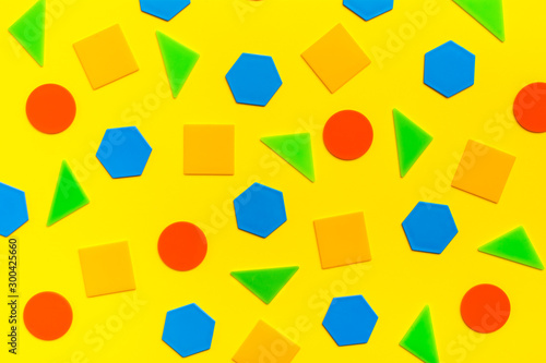 Various flat figures - circles, triangles, squares, hexagons - lie abstractly on yellow cardboard. Colorful bright background.