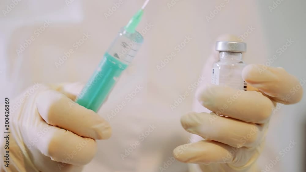 A white-gloved healthcare worker is preparing an injection with a syringe, hypodermic needle and vial. Flu vaccine. A white-gloved healthcare worker is preparing an injection with a syringe, hypodermic needle and vial. Flu vaccine.