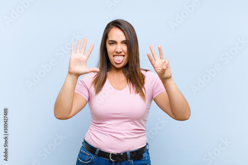 young pretty woman smiling and looking friendly, showing number eight or eighth with hand forward, counting down against blue background photo