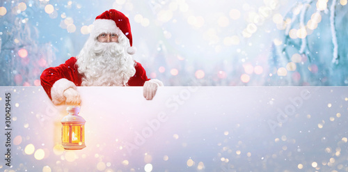 Santa Claus with a Lamp on a Background of a Snowy Forest