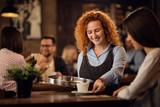 Young happy waitress giving coffee to a woman in a cafe.