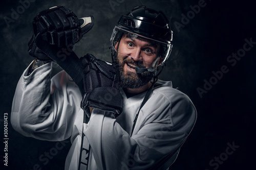 Happy cheerful hockey player has a photo session at dark photo studio.