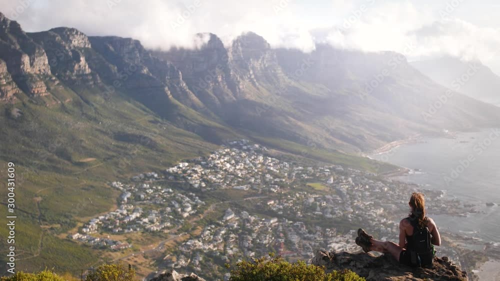 Woman sitting overlooking valley from mountain cliff in Cape Town // wide angle Woman sitting overlooking valley from mountain cliff in Cape Town // wide angle