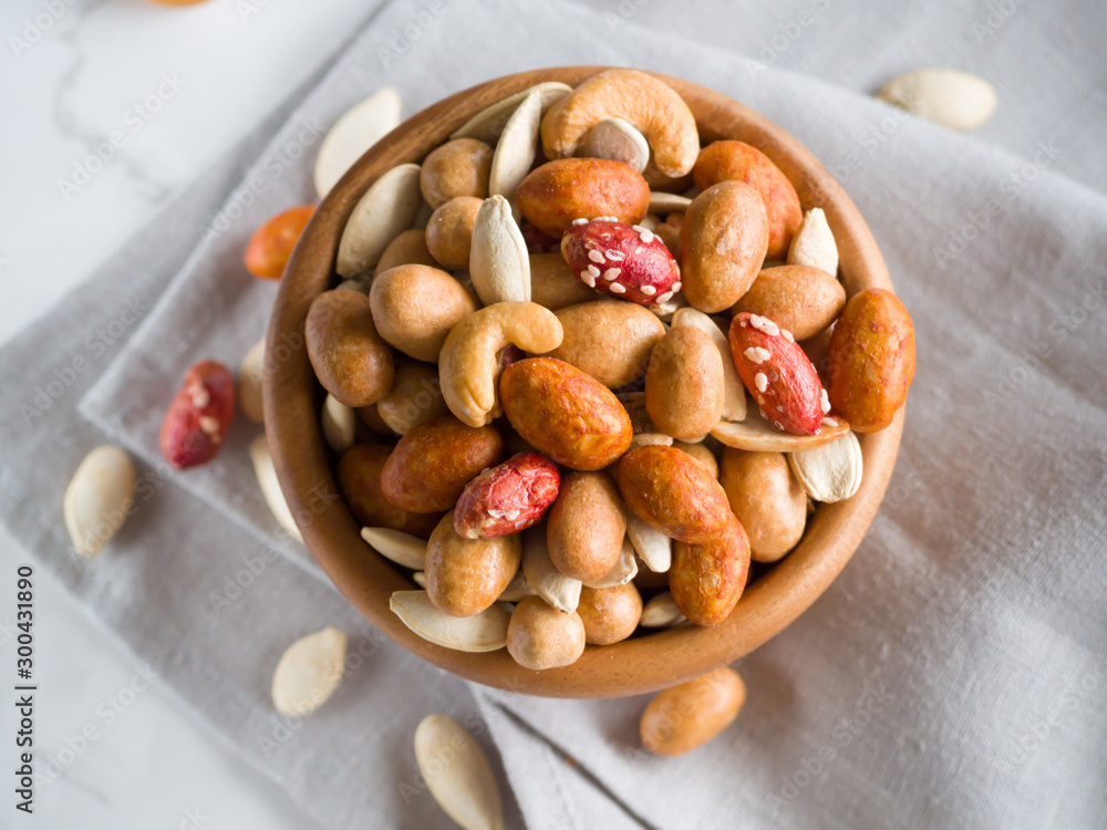 Crispy assorted mixed nuts with different flavors and pumpkin seeds in the wooden bowl and grey linen towel as background. Roasted nuts coated by salt and spicy. Snack for beer. Close up. Top view. Crispy assorted mixed nuts with different flavors and pumpkin seeds in the wooden bowl and grey linen towel as background. Roasted nuts coated by salt and spicy. Snack for beer. Close up. Top view.