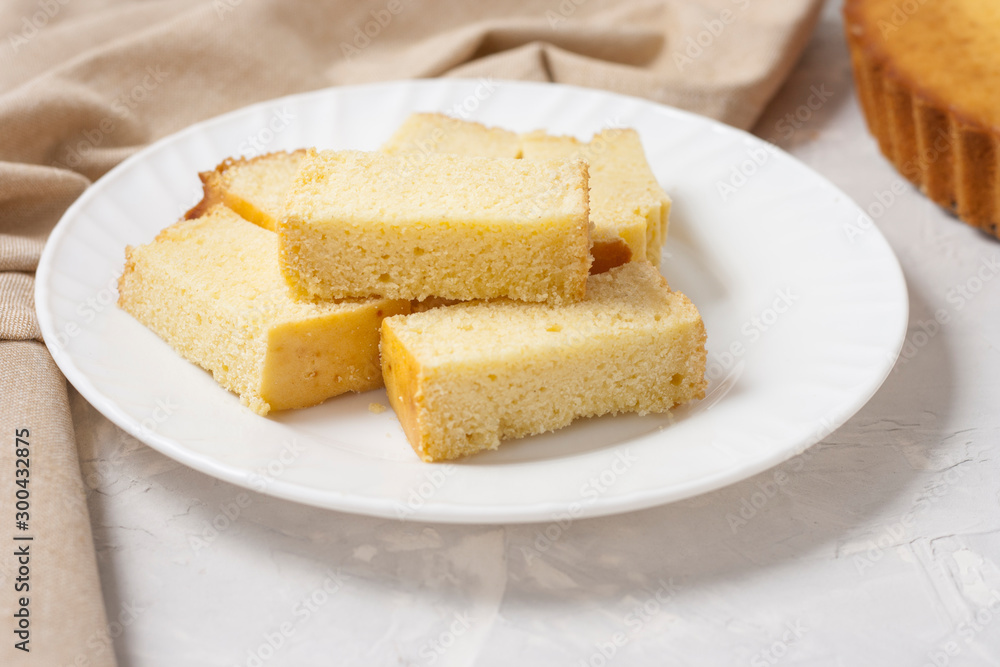 Slices of freshly baked corn bread on a white plate with corn on a light gray background with a linen napkin.