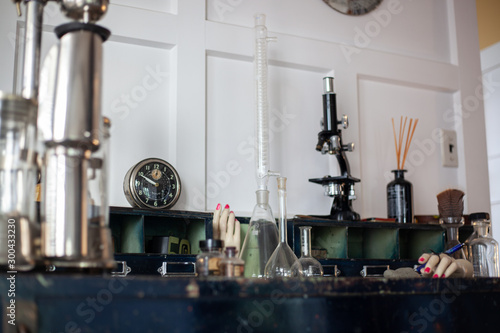 Vintage old things on the table. Glass flasks and test tubes, retro microscope, old round alarm clock with arrows, mannequin hands