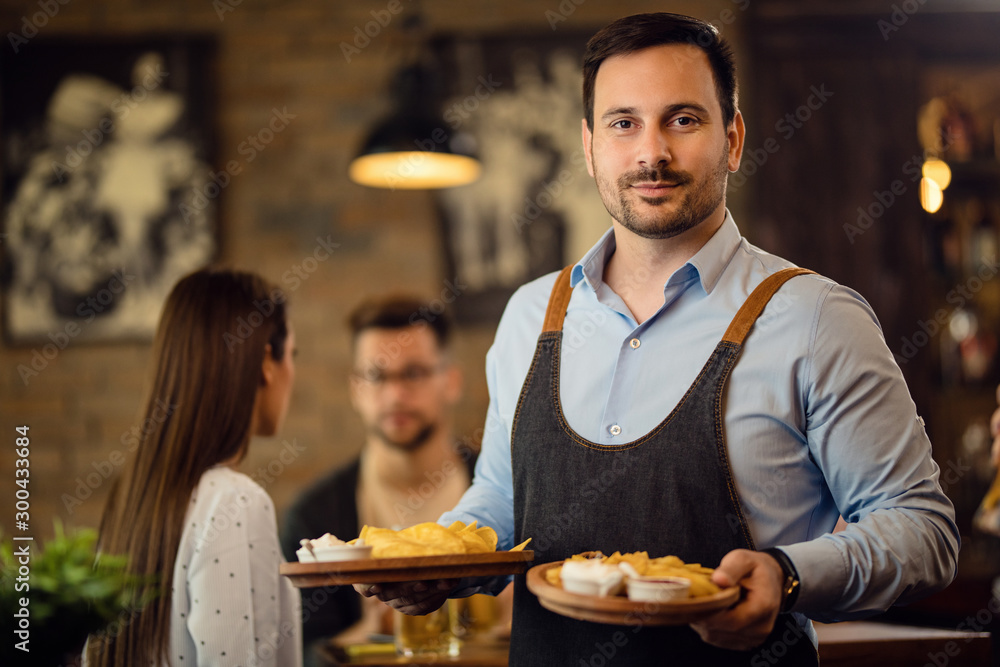 Portrait of smiling waiter serving food in a pub.