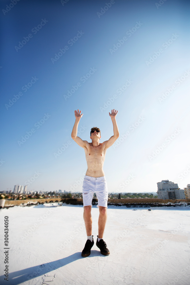 Young attractive man posing in front of camera on the roof of a residential building. Hands up in the air Young attractive man posing in front of camera on the roof of a residential building. Hands up in the air