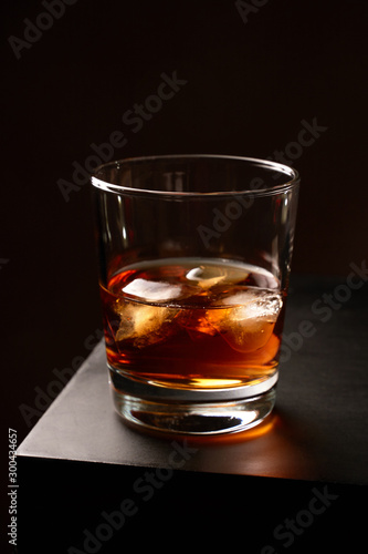 A glass of whiskey with ice on a wooden table. Low key. Vertical orientation.