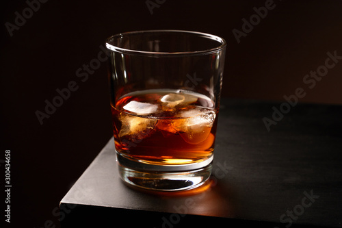 A glass of whiskey with ice on a wooden table. Low key. Horizontal orientation. 