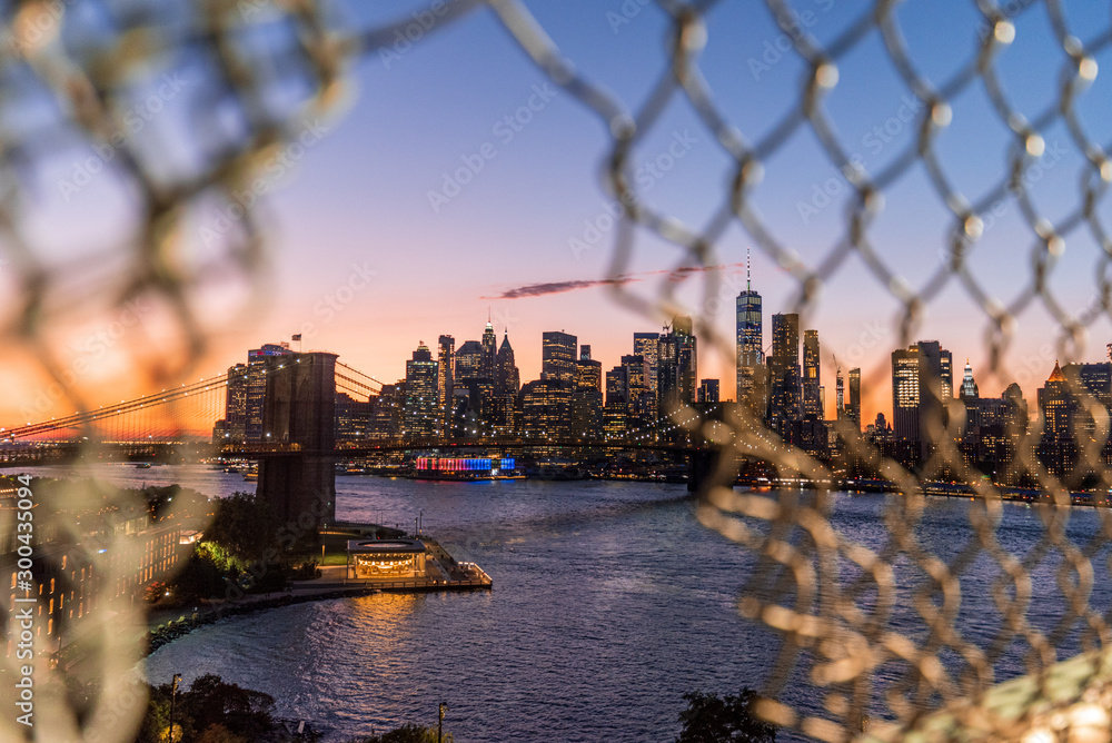 View of Manhattan and the Brooklyn Bridge through a Manhattan Bridge fence opening in the sunset - obrazy, fototapety, plakaty 
