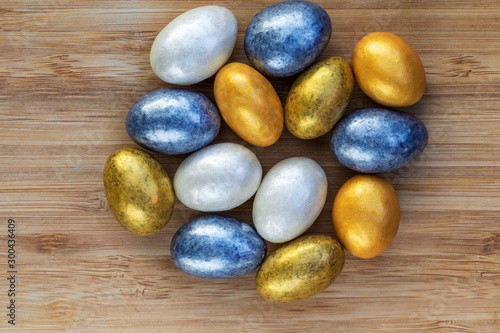 Almonds in yellow, silver, gold and white glaze lie in the center on a brown wooden surface