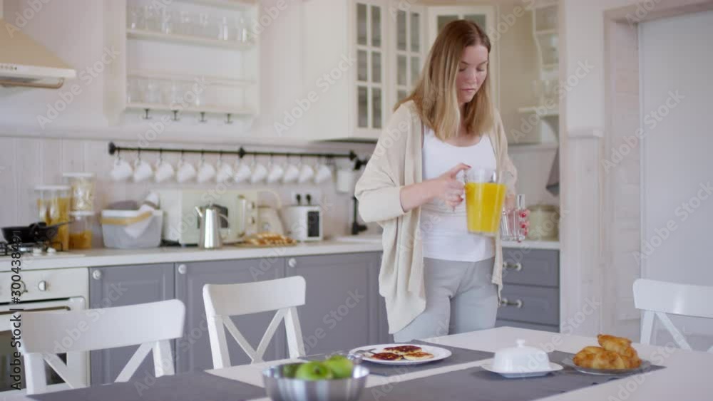 Tracking of attractive woman pouring orange juice into glass and sitting down to eat pancakes in morning Tracking of attractive woman pouring orange juice into glass and sitting down to eat pancakes in morning