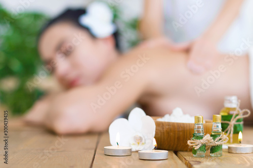 Closeup burning candles, bottles with aroma oil, bowl with salt. Young pleased woman is getting thai massage, therapy. Brunette girl is lying on couch in spa ayurveda salon. Relax and health care.