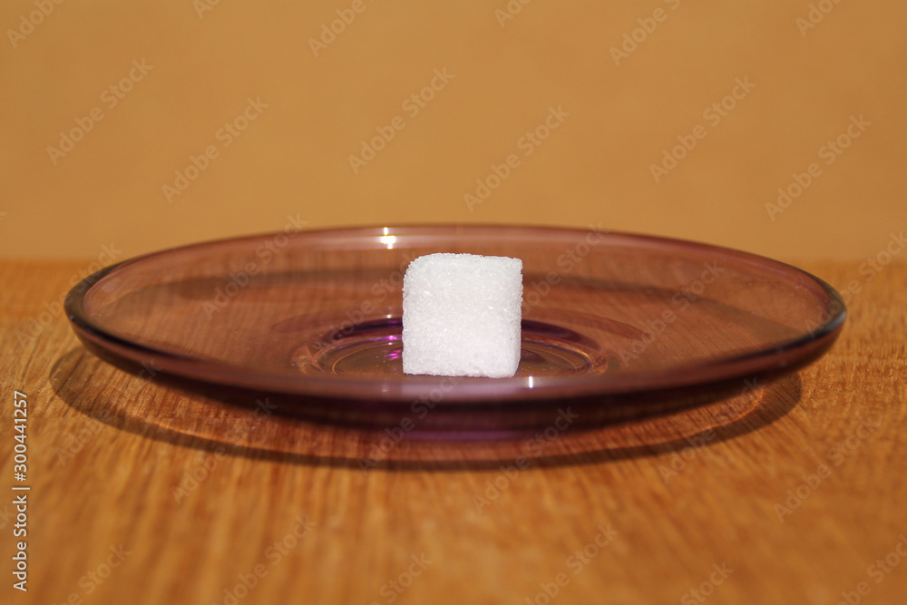 Obraz premium one white sugar cube on a plate, concept of excess sugar intake, diabetic, close-up, copy space