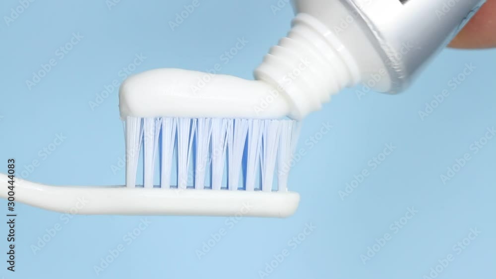 Putting toothpaste on a brush on blue background Putting toothpaste on a brush on blue background