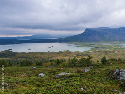 View on meandering river delta at Rapadalen valley in Sarek national park, Sweden. Lapland mountains, rocks and birch trees. Early autumn colors, moody sky with clouds. photo