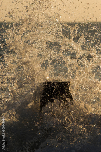 A Wave crashes over a groyne at sunset taken on Southwick Beach, West Sussex, United Kingdom.