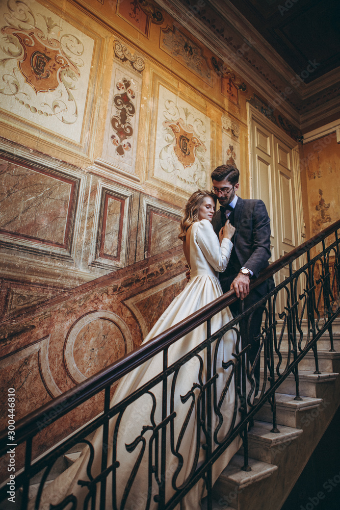 stylish wedding couple of pretty bearded groom and elegant blonde woman in wedding dress posing for photo in chic palace, copy space, noise effect stylish wedding couple of pretty bearded groom and elegant blonde woman in wedding dress posing for photo in chic palace, copy space, noise effect