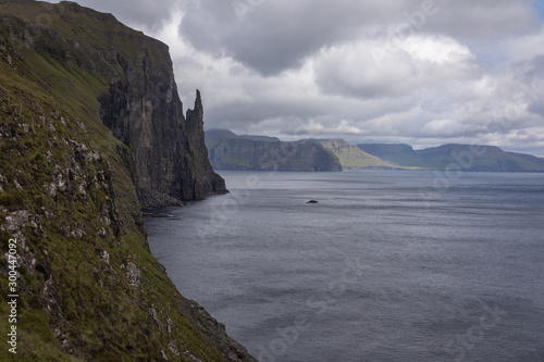 Beautiful view of Trollkonufingur (Witch's Finger) Fjord appear from clouds in blue sky next to North Atlantic ocean, hiking from Sandavagur village on Vagar island of the Faroe Islands.