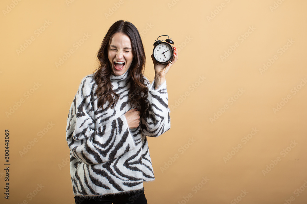 Fototapeta premium Image of a young beautiful woman posing isolated against an orange wall holding an alarm clock