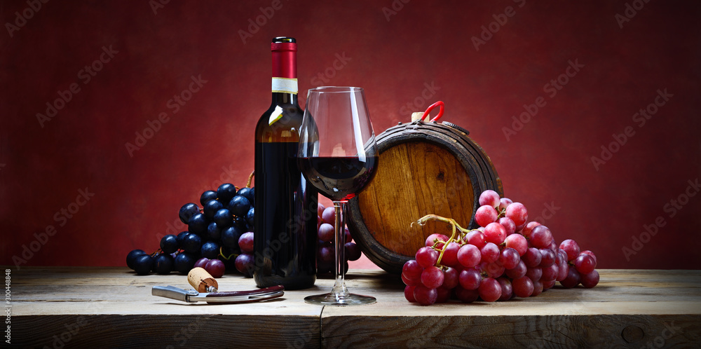 Red wine glass with bunches of grapes, bottle and small barrel. Space for text.