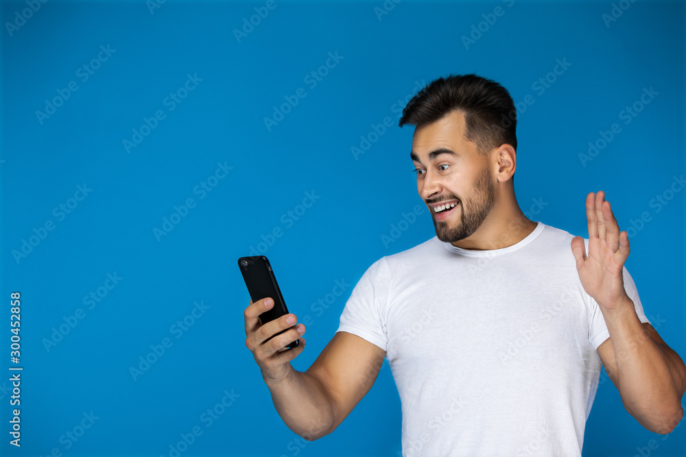 Cute european man smiles at the phone and waves his hand Cute european man smiles at the phone and waves his hand