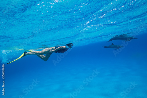 woman swimming with a pod of Spinner dolphins (Stenella longirorstris) over sand in Sataya reef, Egypt, Red Sea photo