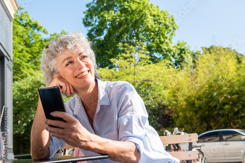 smiling middle aged woman sitting outside on sunny day looking with cellphone