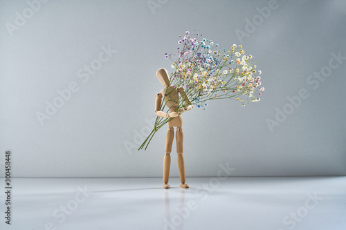 Wooden man with a branch of delicate flowers on a light gray background