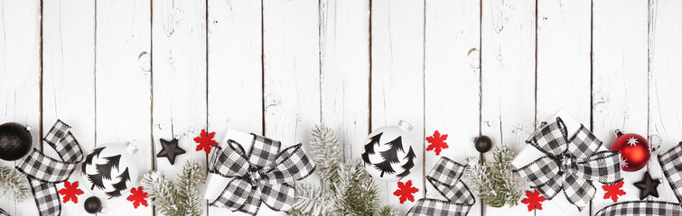 Christmas banner of black and white checked buffalo plaid ribbon, gifts and ornaments. Above view long bottom border on a white wood background.