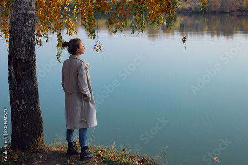 Fényképezés Youing girl wearing a beige trench coat, jeans and black boots, standing and looking to the beautiful landscape